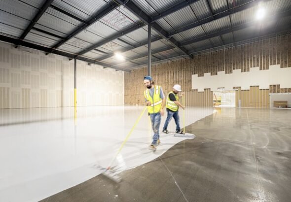 Professional applying epoxy resin flooring with roller on concrete garage floor during DIY installation process