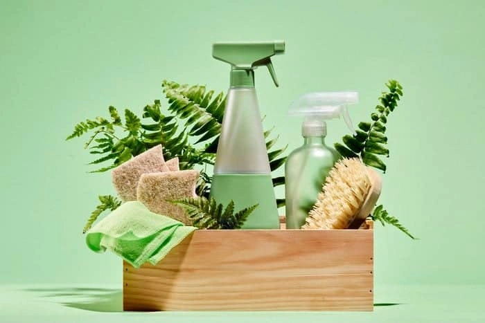 7 Sustainable Home Cleaning Practices for Healthier Living 5 Sustainable home cleaning products featuring reusable spray bottles and natural brushes arranged in wooden crate with green ferns