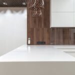 White epoxy countertops on a modern kitchen island with white cabinets, wood panel backsplash, and pendant light