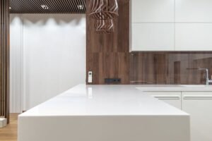 White epoxy countertops on a modern kitchen island with white cabinets, wood panel backsplash, and pendant light
