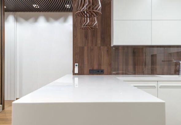 White epoxy countertops on a modern kitchen island with white cabinets, wood panel backsplash, and pendant light