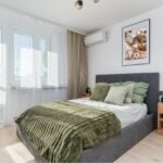 Small master bedroom ideas with grey upholstered bed, green bedding, wooden nightstand and sheer curtains