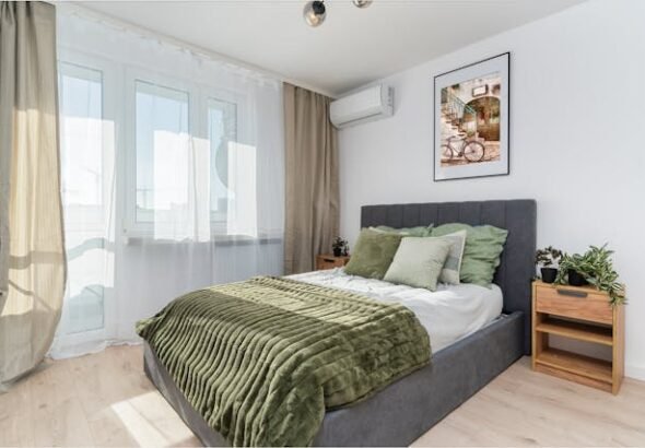 Small master bedroom ideas with grey upholstered bed, green bedding, wooden nightstand and sheer curtains